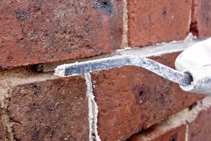 Close up of red brick wall with section of mortar being replaced with a hand tool