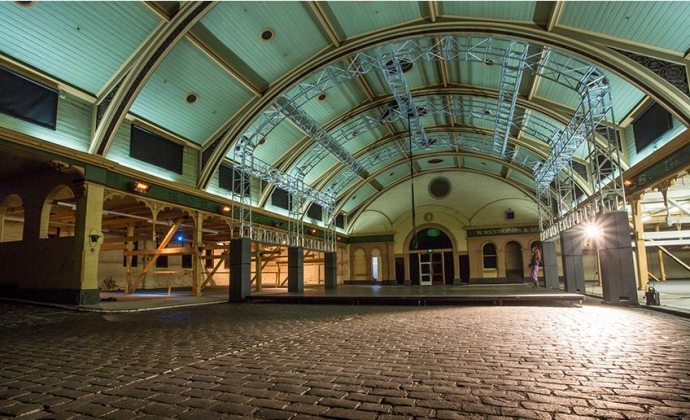A large empty room with cobble stone floor, a colourful painted wooden arched roof.